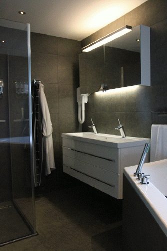 Detail van de afgewerkte badkamer met inbouwkraan en donkere vloertegels.