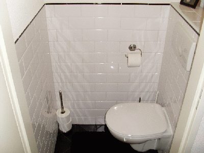 Gerenoveerd toilet met witte metrotegels, zwarte vloer en een hangend toilet.